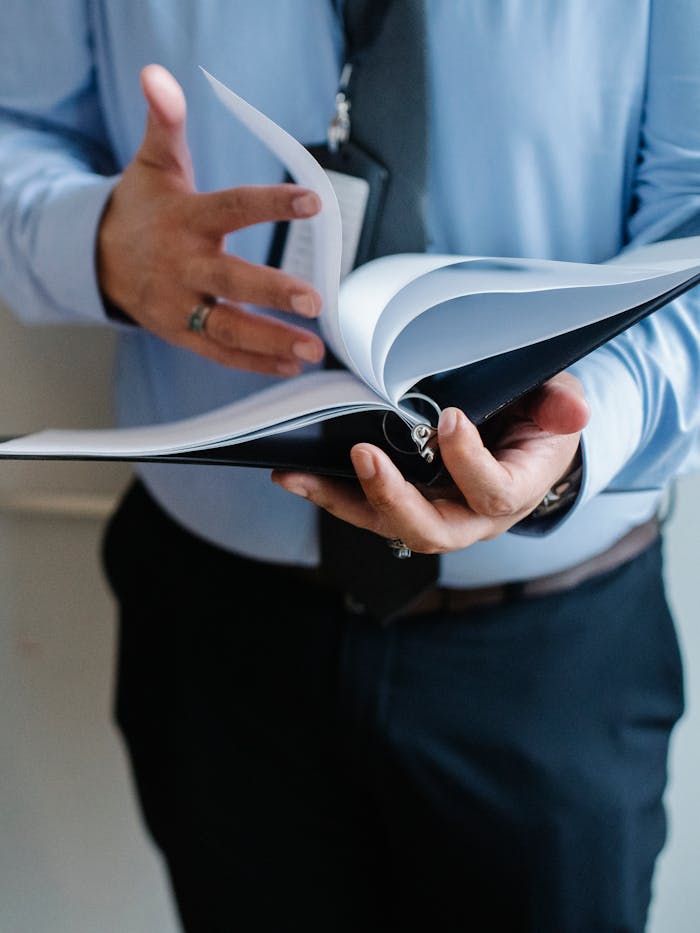 Crop unrecognizable businessman in formal suit flipping through documents in folder in office
