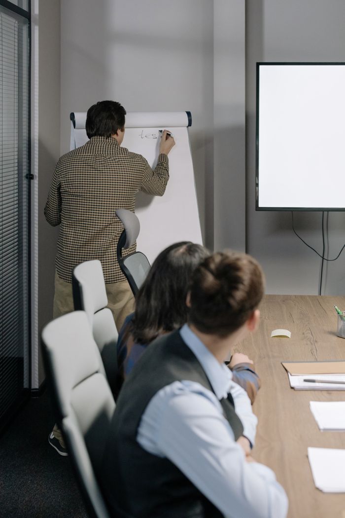 who-we-are Three colleagues collaborating during an office meeting with a whiteboard discussion.
